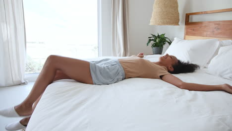 relaxing at home, woman lying on bed with arms stretched, looking content