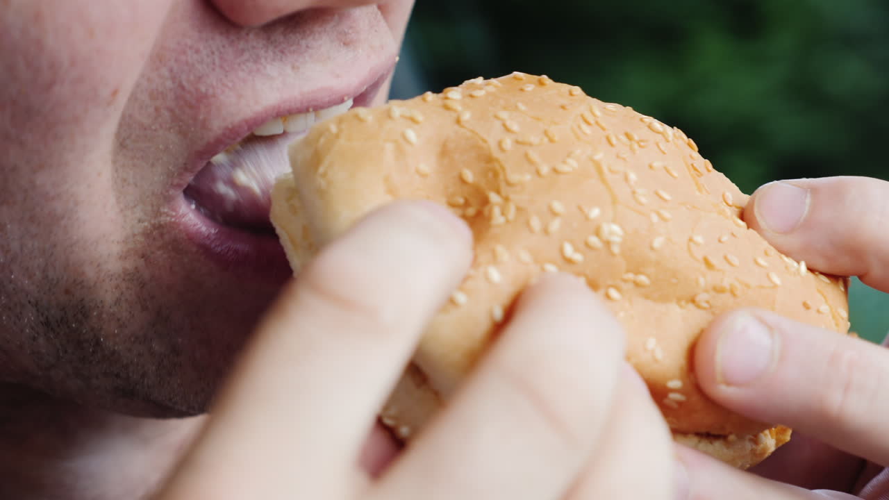 boca de un macho adulto comiendo con avidez una hamburguesa de cerca