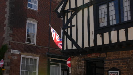 Antiguo-Pub-Tudor-Británico-En-La-Esquina-De-Una-Calle-Con-La-Bandera-Union-Jack-Ondeando-Afuera