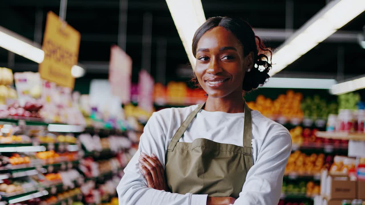 A confident grocery worker smiles with arms crossed in a vibrant supermarket