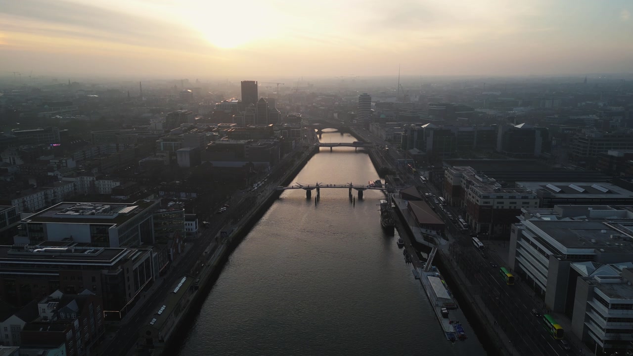 aerial view flying over Liffey River in the heart of Dublin City centre featuring different bridges and a golden dusty sunset, - Dublin, Ireland
