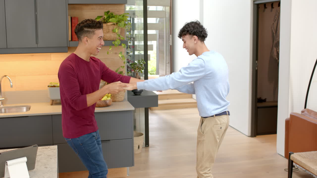 Dancing , multiracial gay couple enjoying time in modern home kitchen