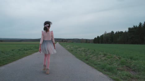 little girl in ballerina dress walking happily down field road