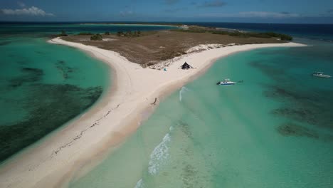 A-tropical-island-with-turquoise-waters,-a-boat,-and-a-beach-tent,-aerial-view