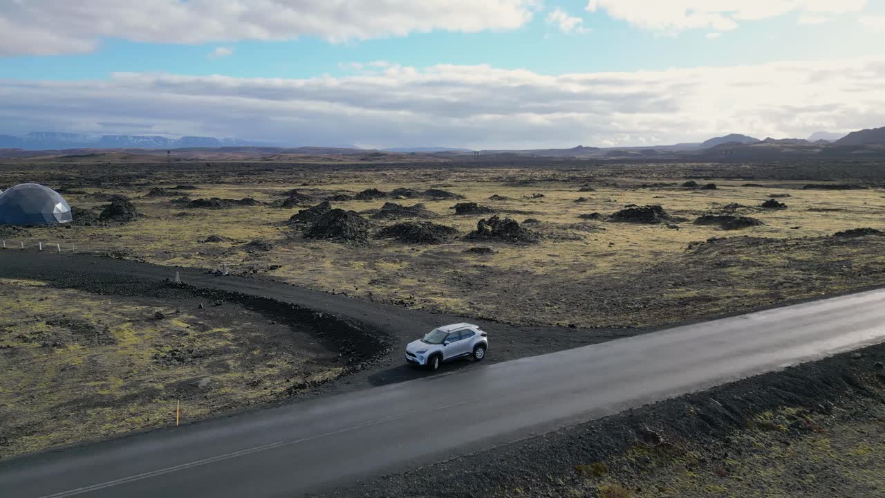 Imagine-se a planar sobre a Islândia, observando um carro a navegar por musgo e terreno vulcânico, emoldurado por picos nevados sob um céu azul-celeste impecável, alimentando o seu desejo de aventura