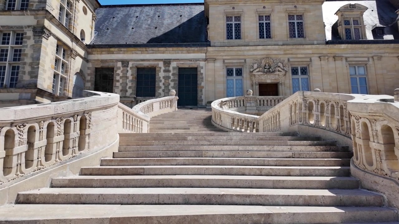Ripresa al rallentatore mentre si sale la Scalinata a Ferro di Cavallo al Castello di Fontainebleau, evidenziando l'architettura rinascimentale del palazzo e il cortile storico in Francia