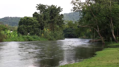 4k beautiful wide angle shot of a river with rope swing hanging from a tree in thailand