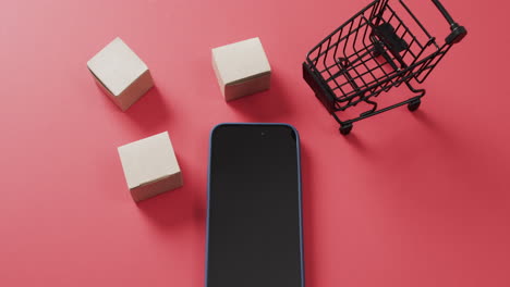 video de un teléfono inteligente con pantalla en blanco, cajas, carrito de compras sobre fondo rojo