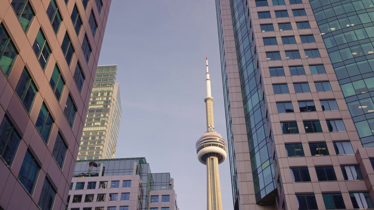 Câmera se move lateralmente da direita para a esquerda com a CN Tower enquadrada entre edifícios de escritórios do centro