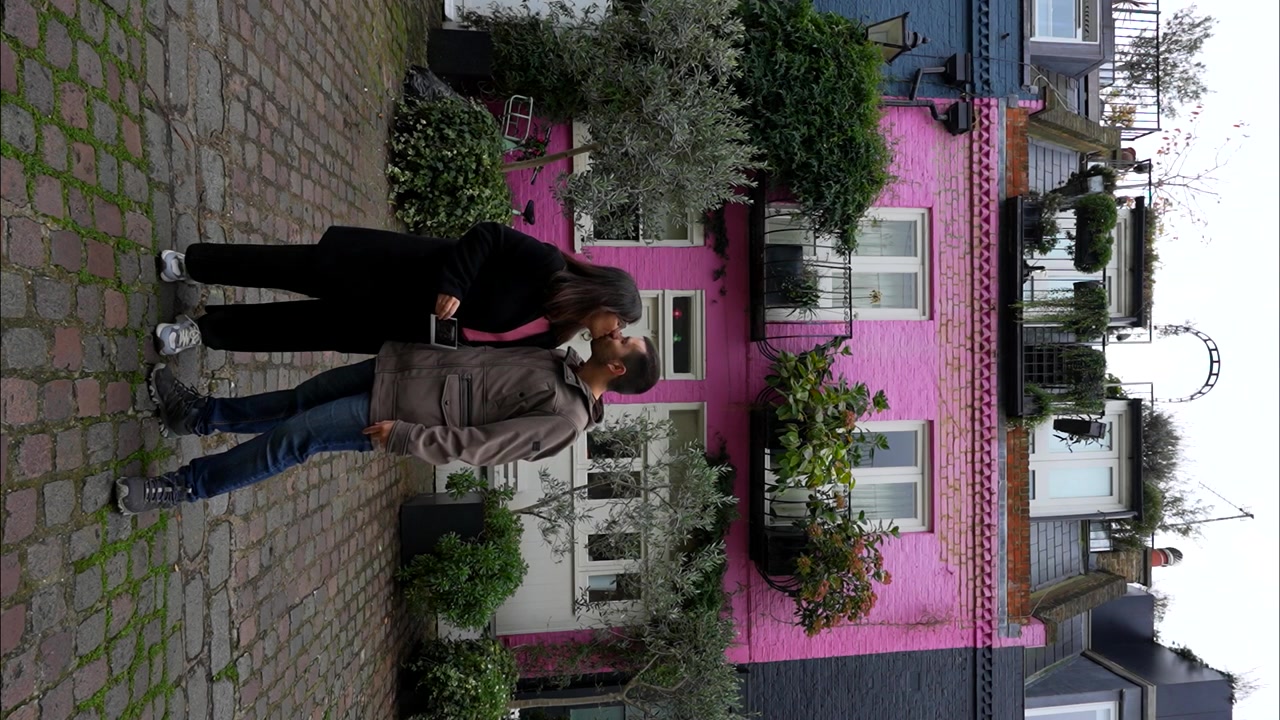 Couple heureux montrant une échographie de leur futur bébé devant une maison rose. Vertical.