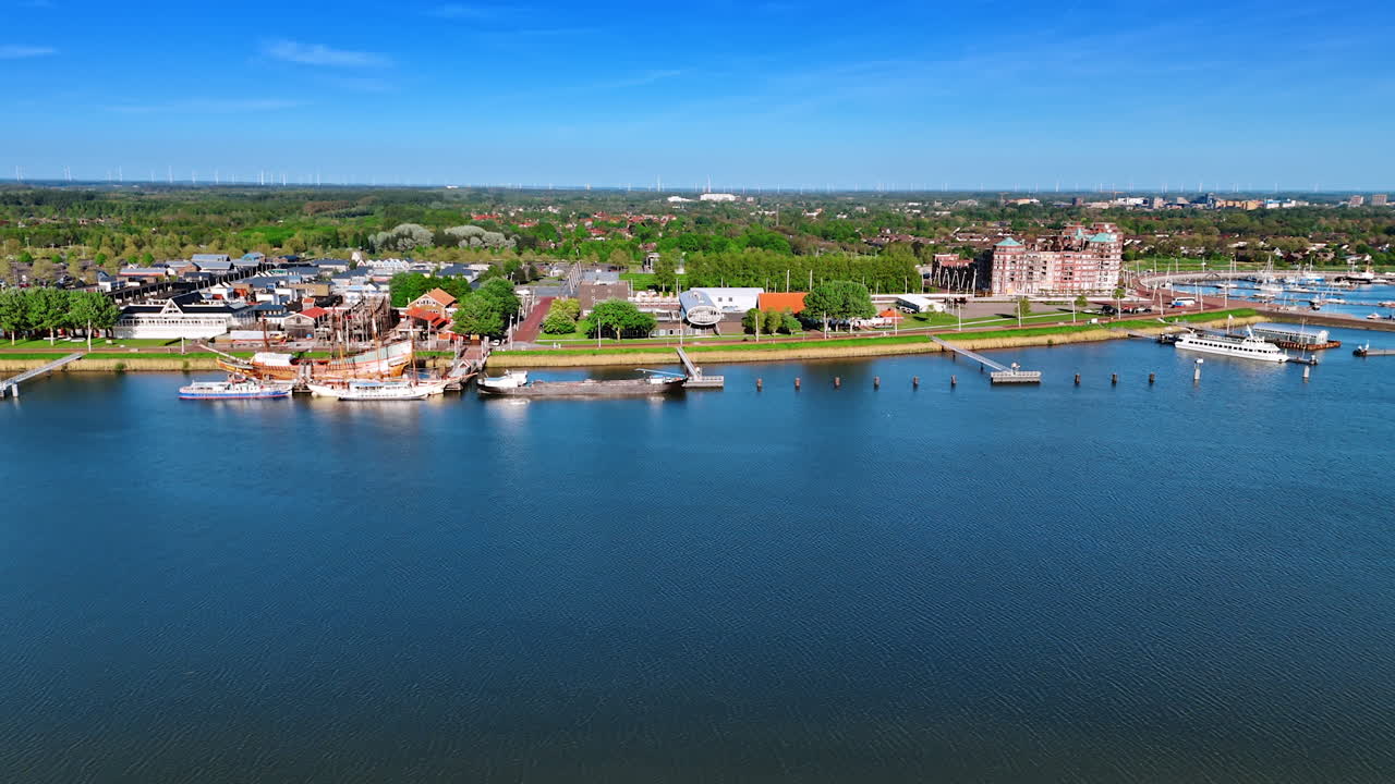Approaching a beautiful waterfront of the Markermmer lake, Lelystad,the Netherlands. Large ship Batavia at Museum Batavialand is at the pier. Aerial view.