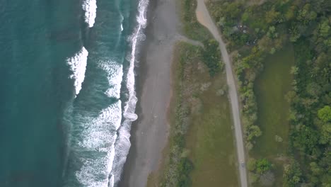 Top-down-dorne-shot-panning-over-the-waves-breaking-on-the-beach-and-lush-green-hills