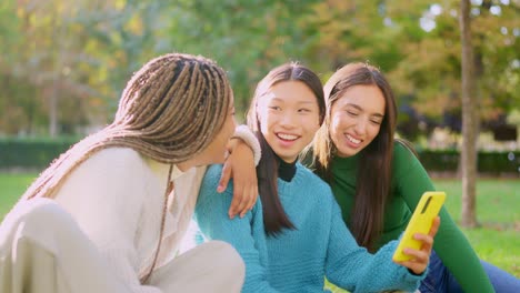 three happy young women sharing a moment and looking at a smartphone in a park