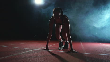 Female-athlete-on-a-dark-background-is-preparing-to-run-the-cross-country-sprint-from-the-pads-on-the-treadmill-on-a-dark-background