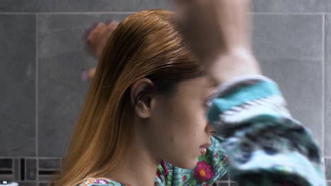 Side-view-of-Young-Asian-Indian-female-using-both-hands-to-comb-hair-in-bathroom