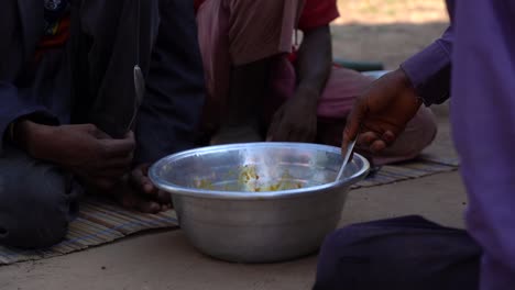 many african man are sharing a meal out of one pot on the ground of their village in rural ghana