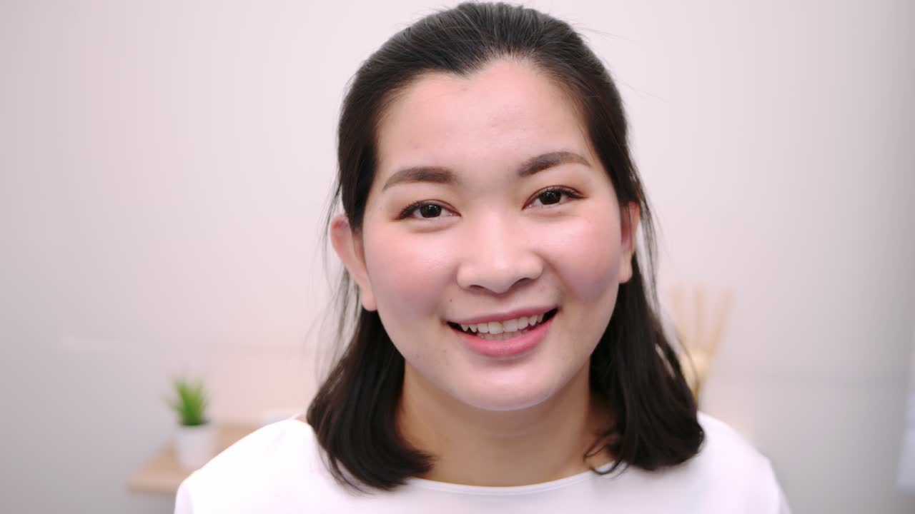 아름답고 웃고 있는 아시아 여성들은 휴일에 혼자 전문적인 초상화를 취한 카메라를 바라보며 극도로 자신감 있는 젊은 얼굴을 하고 맑은 빛, 슬로우 모션 장면으로 휴식을 취합니다.