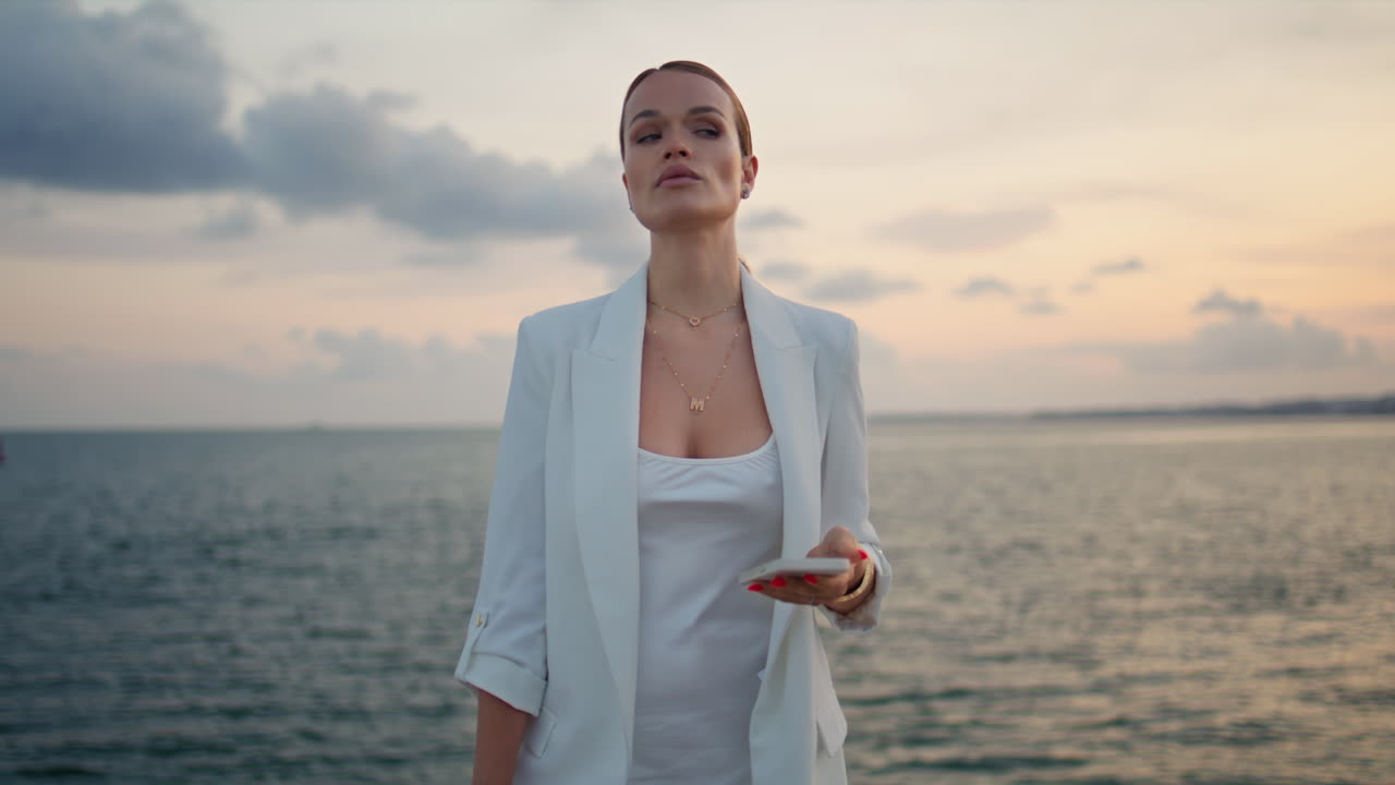la señora jefe con el teléfono inteligente de pie en la hermosa playa de la noche de cerca.