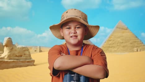 asian boy with a hat and binoculars crossing arms and smiling to camera while traveling in giza pyramid. boy researcher examines something, travel adventure concept, close up