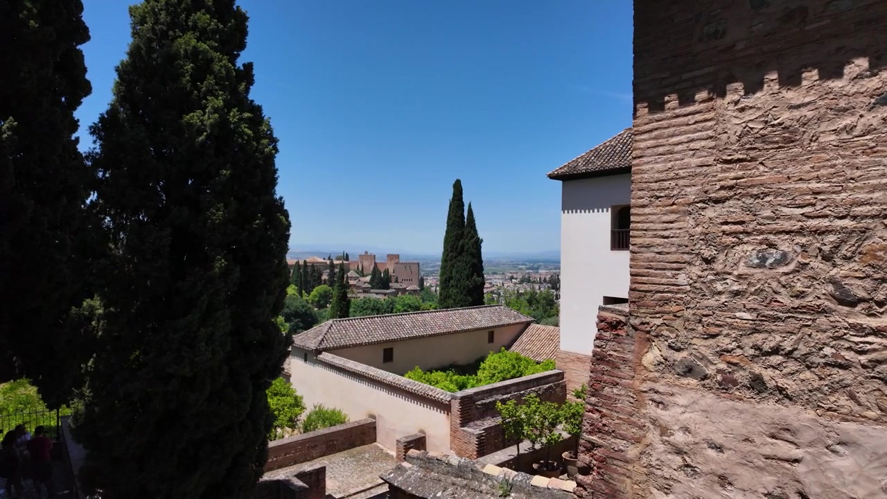 Vista al rallentatore delle mura della fortezza dell'Alhambra con cipressi e Granada visibile in lontananza in una giornata limpida in Spagna