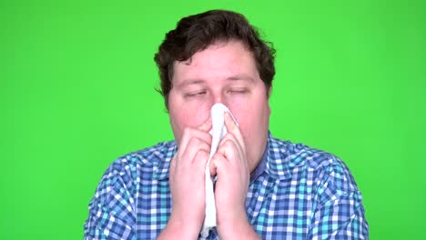 portrait of young man in plaid shirt with allergy or cold, blowing his nose with a tissue, isolated green screen.