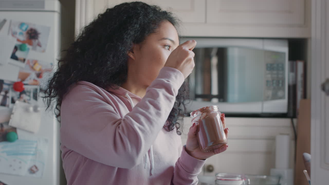 una adolescente furtiva comiendo chocolate esparcido de un frasco en la cocina disfrutando de un delicioso regalo una adolescente descarada consumiendo bocadillos poco saludables en casa