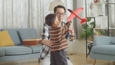 asian father and son playing toy plane together at home