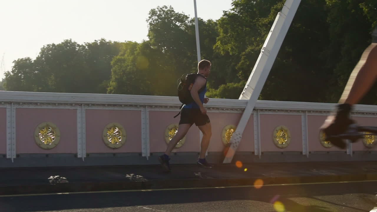 Athletic Man With Black Backpack Running At The Concrete Bridge In London, England - Slow Motion Pan Left Shot