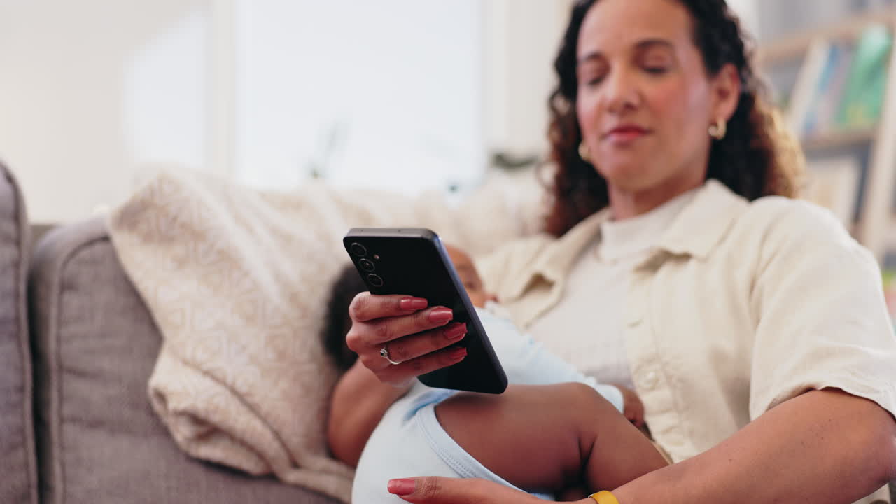 madre usando el teléfono móvil mientras sostiene al bebé en el sofá