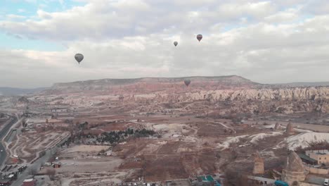 Hot-air-balloons-fly-over-Goreme-Valley-in-Cappadocia,-Turkey---Ascending-Wide-Aerial