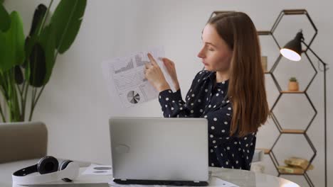 una joven segura lleva a cabo webinars, entrenamientos de negocios en línea. un entrenador en línea muestra gráficos frente a una computadora portátil y explica algo a una audiencia en línea