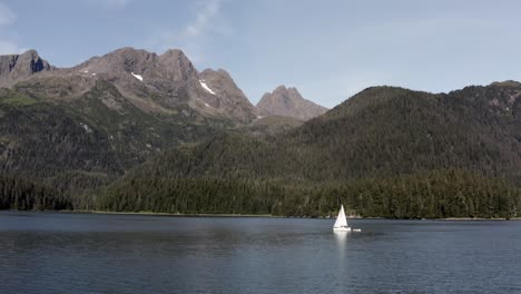 Velero-Solitario-Navegando-En-El-Mar-Con-Vistas-Panorámicas-De-Las-Montañas-Y-Los-Bosques-En-Alaska,-Ee.uu.