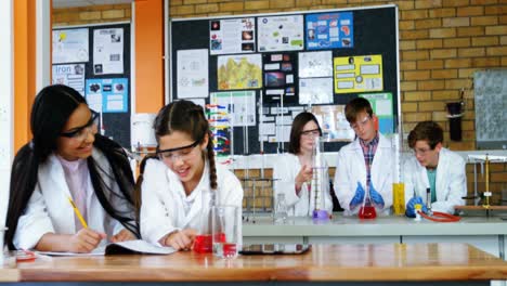 niñas escolares escribiendo en un libro de diario mientras experimentan en el laboratorio en la escuela