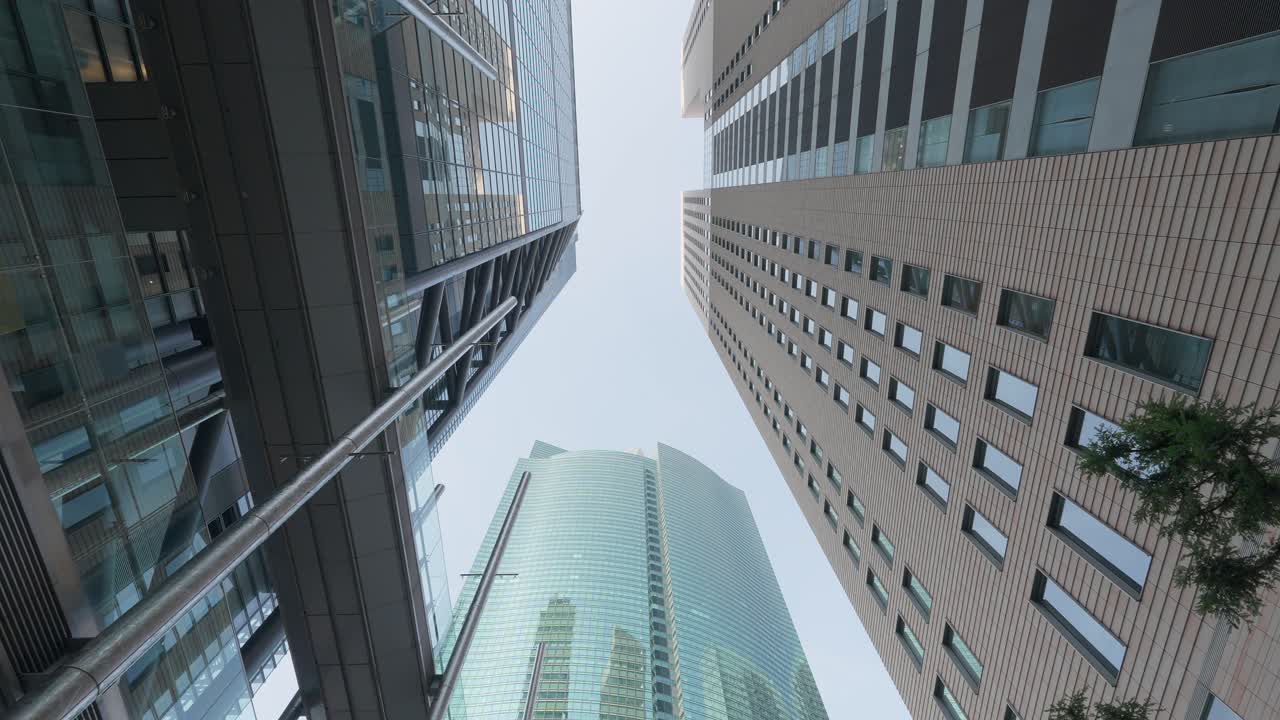 Looking up at a cluster of tall, contemporary office buildings in a bustling urban financial district