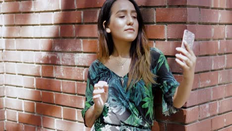 Woman-leaning-on-a-brick-wall-using-a-mobile