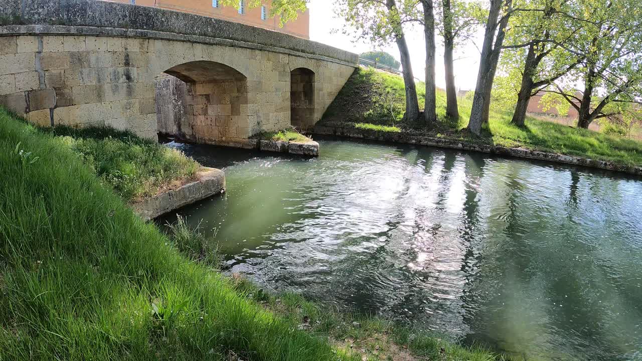Acqua del canale che scorre placidamente sotto un vecchio ponte di pietra in primavera.