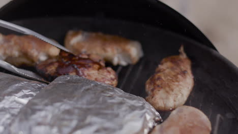 Flipping-barbecue-chicken-with-metal-tongs-on-a-charcoal-black-kettle-grill-at-a-public-park-in-summer