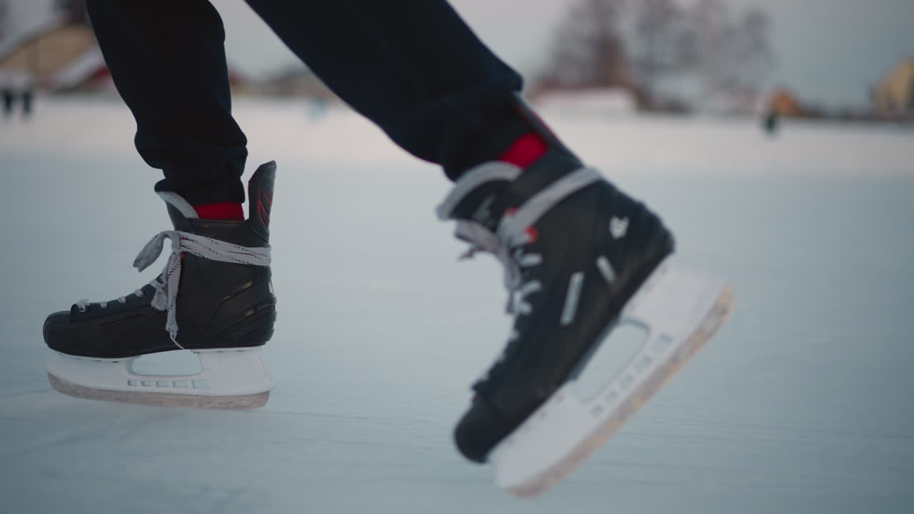 legs of skater gliding on ice rink with blurred backdrop of people skating on snow covered surface under soft winter light outdoor scene capturing movement and grace against cold atmosphere