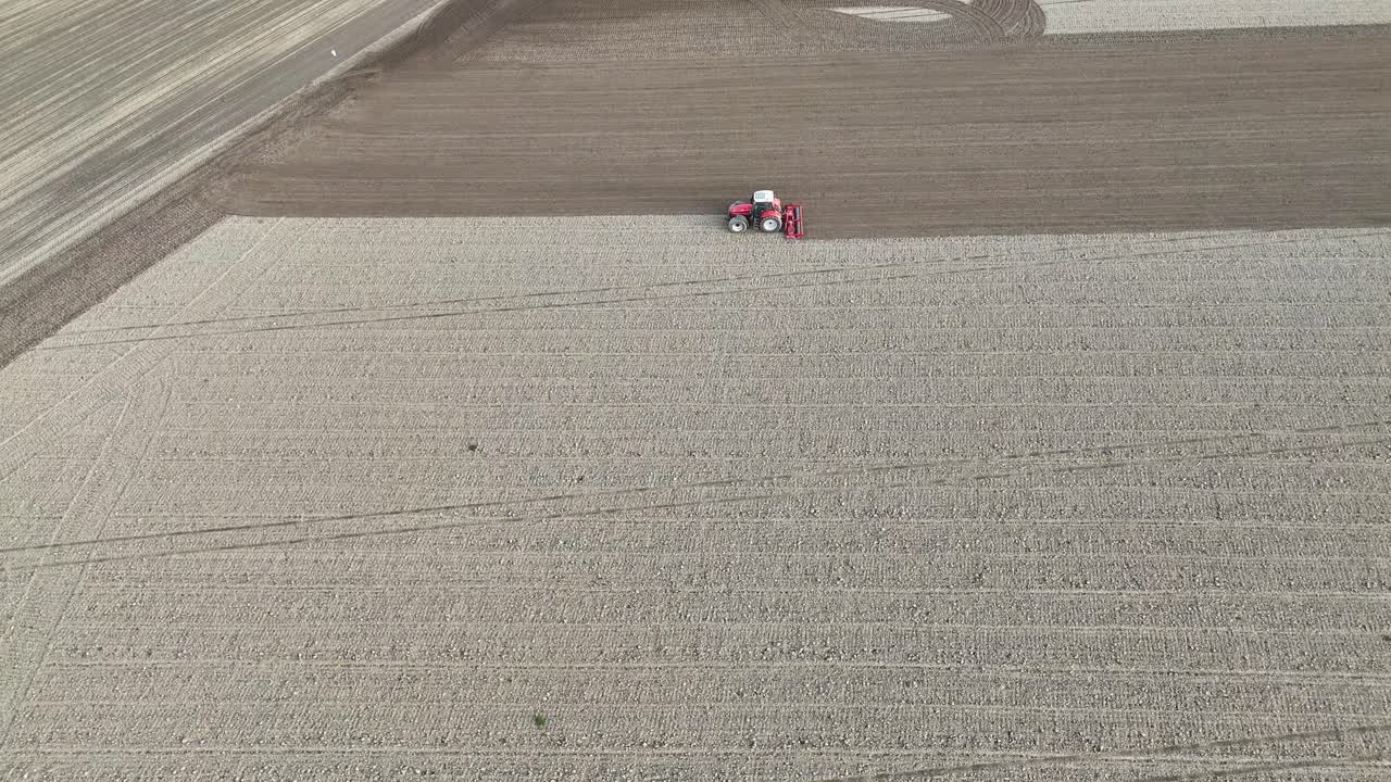 Drone performs a slow orbit around a tractor plowing fields in Olza, Piacenza, highlighting the contrast between freshly tilled soil and untouched areas in precise agricultural geometry, slow motion