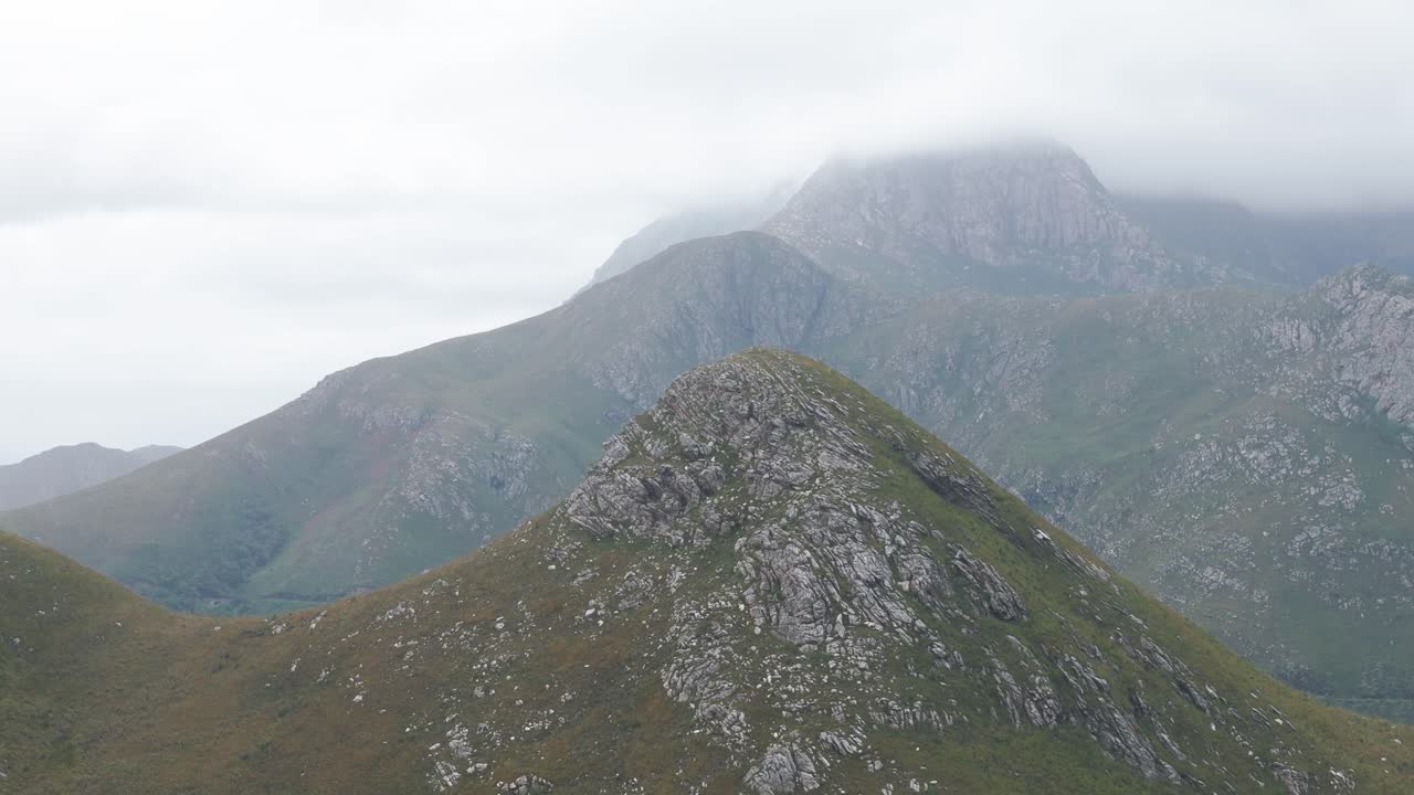 fotografía aérea de un pico de montaña en el paso de outeniqua, cabo occidental, sudáfrica. el avión no tripulado se mueve hacia adelante, panorámica sobre el pico, con un telón de fondo de montaña nublado creando una escena dramática y brumosa