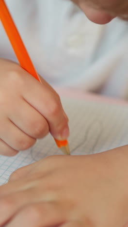 schoolchild draws abstract picture with graphite pencil in checkered exercise book at desk closeup. toddler boy does creative task at art lesson