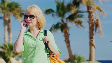 Touristin-Mit-Sonnenbrille,-Die-Auf-Dem-Hintergrund-Von-Himmel-Und-Palmen-Telefoniert