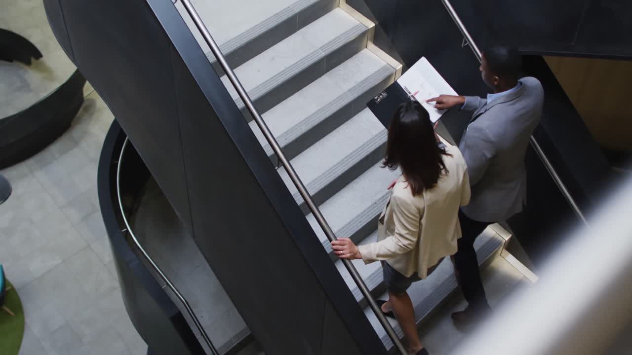 Empresário e empresária diversos conversando enquanto descem escadas de um escritório moderno