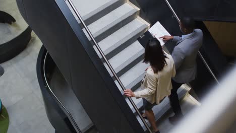 Diverse-businessman-and-businesswoman-talking-and-talking-down-stairs-of-modern-office