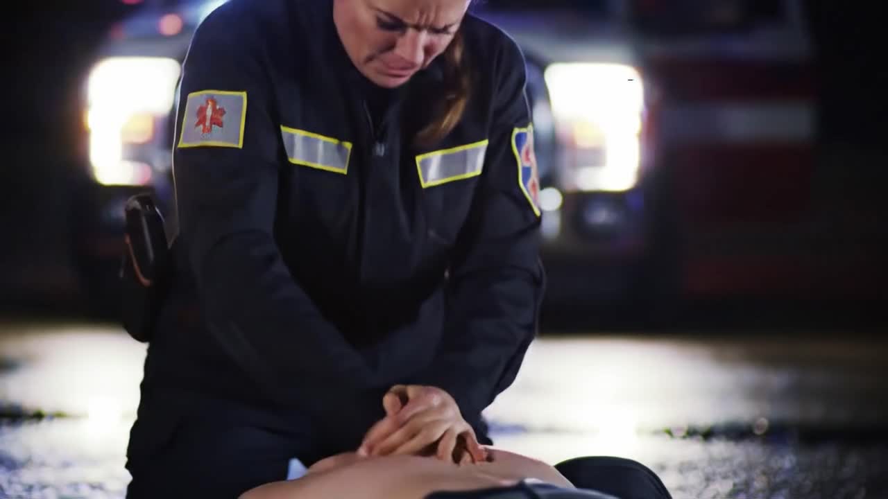 An emergency responder administers CPR on an individual in distress at night while sirens wail in the background. The scene highlights the urgency and dedication of medical professionals.