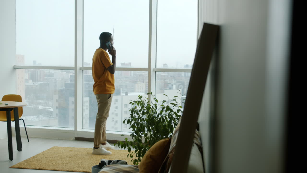 Man talking on phone by window in apartment