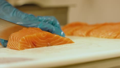 cámara lenta de una jugosa pieza de salmón siendo cortada por un chef en un restaurante y luego colocada entre otras rebanadas
