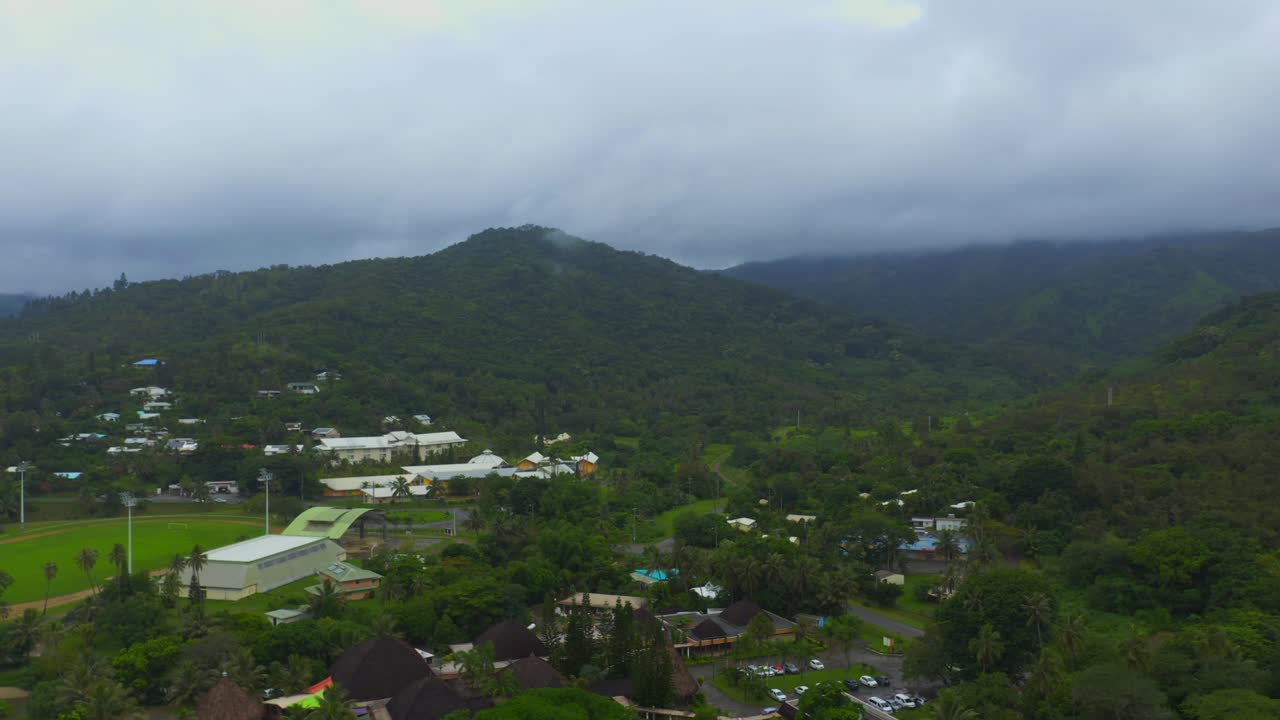 disparo elevado que se retira de un área urbana enclavada en una exuberante vegetación tropical y una hermosa playa costera durante un día lluvioso