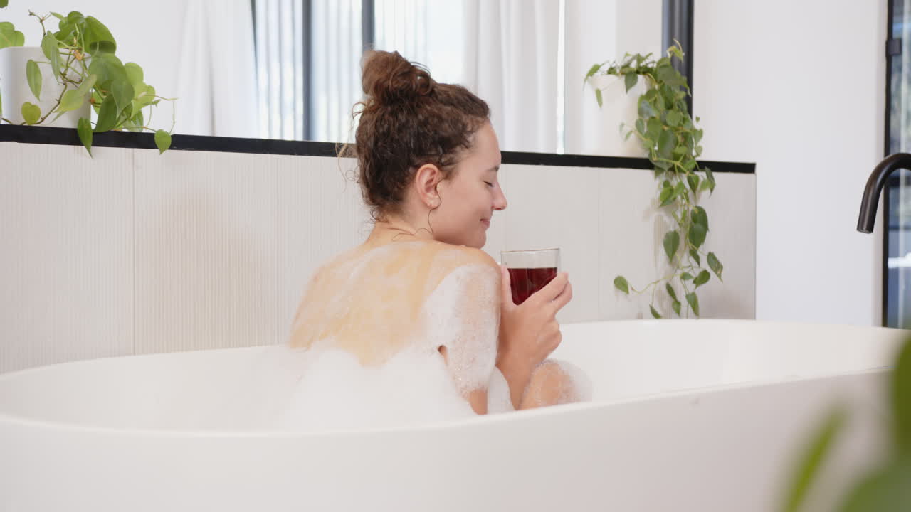 Relaxing in bathtub, woman enjoying bubble bath and holding glass of wine