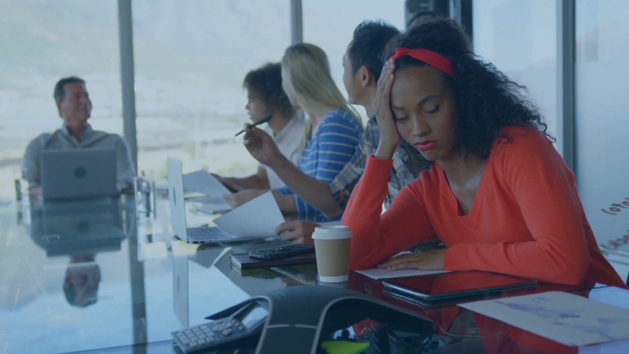 Donna in rosso che riposa mentre il responsabile aziendale parla, il laptop proietta testo su un vetro e il team discute documenti.